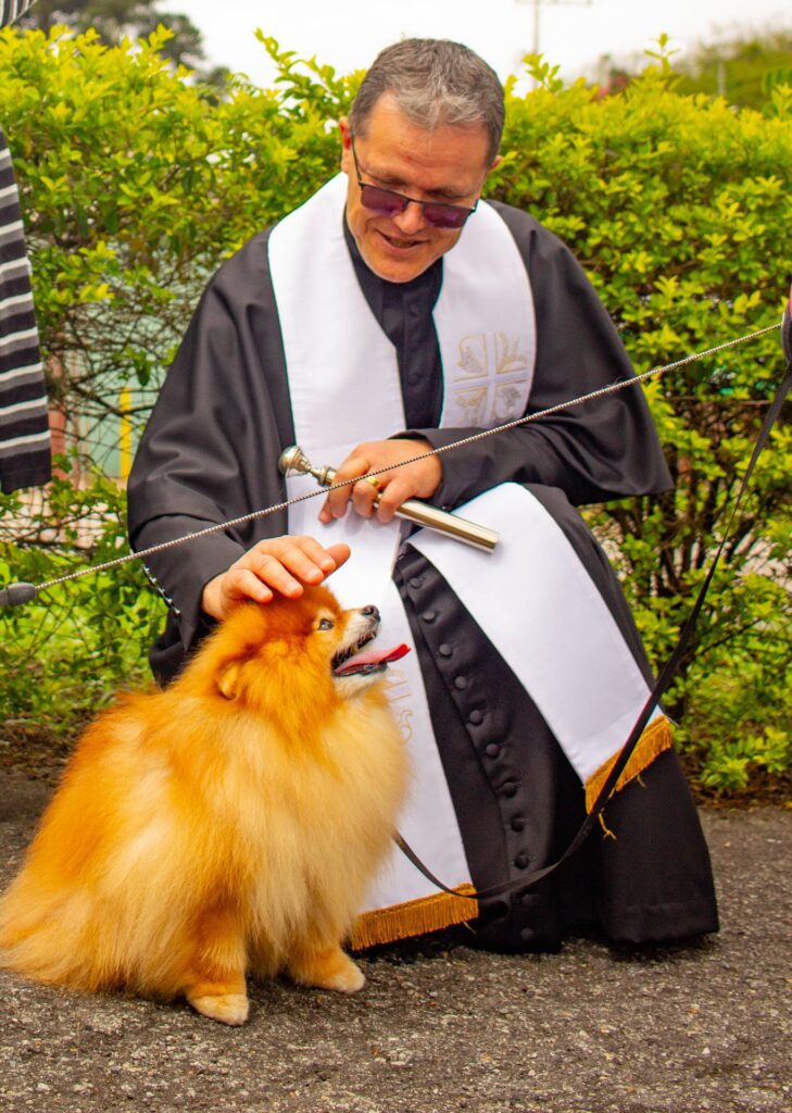 Padre ajoelhado abençoa um cão da raça lulu-da-pomerânia durante a Bênção dos Animais na Paróquia Imaculada Conceição